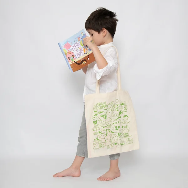 Niño sostendiendo un libro y una Totebag con ilustración en verde de Cuentos en Pijamas.