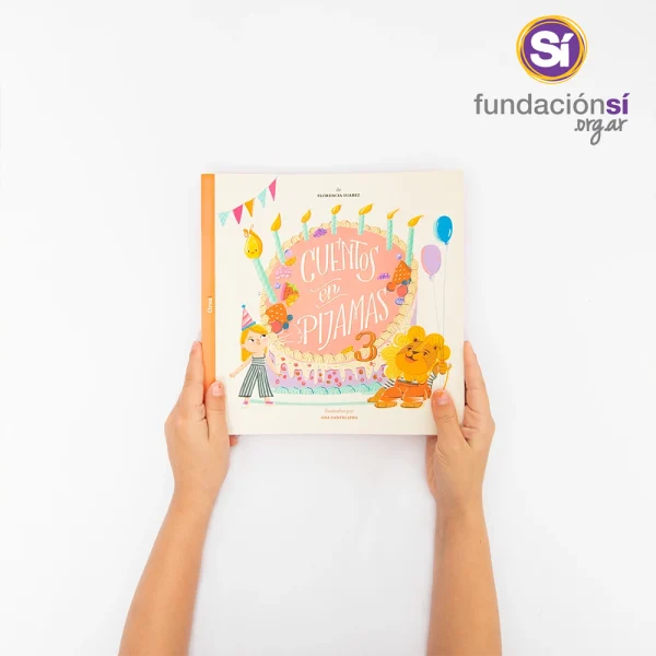 Dos manos infantiles sostienen el libro “Cuentos en Pijamas 3”. La portada muestra una torta de cumpleaños.