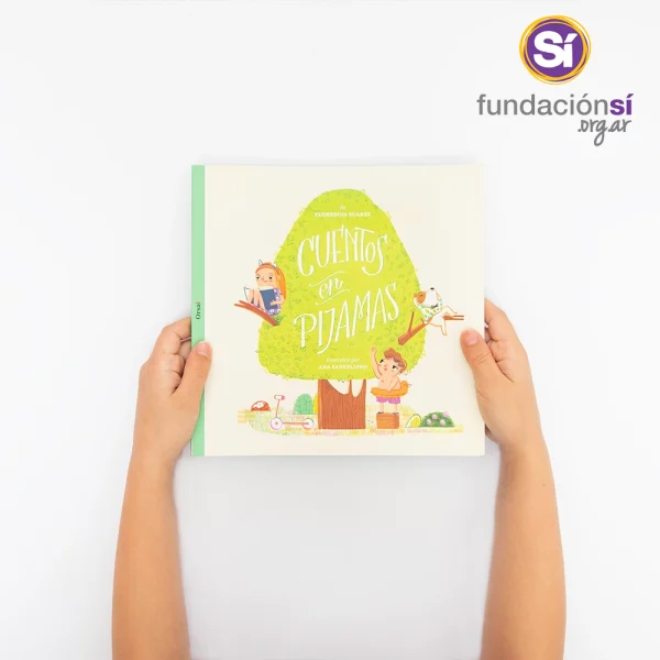 Dos manos infantiles sostienen el libro “Cuentos en Pijamas 1”. La portada muestra un árbol, una niña, un niño y un perrito.